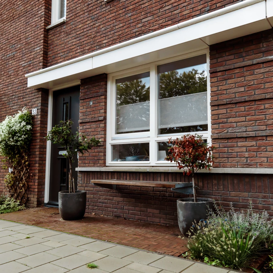 Voortuin met bankje, twee grote potten en border met klimplant